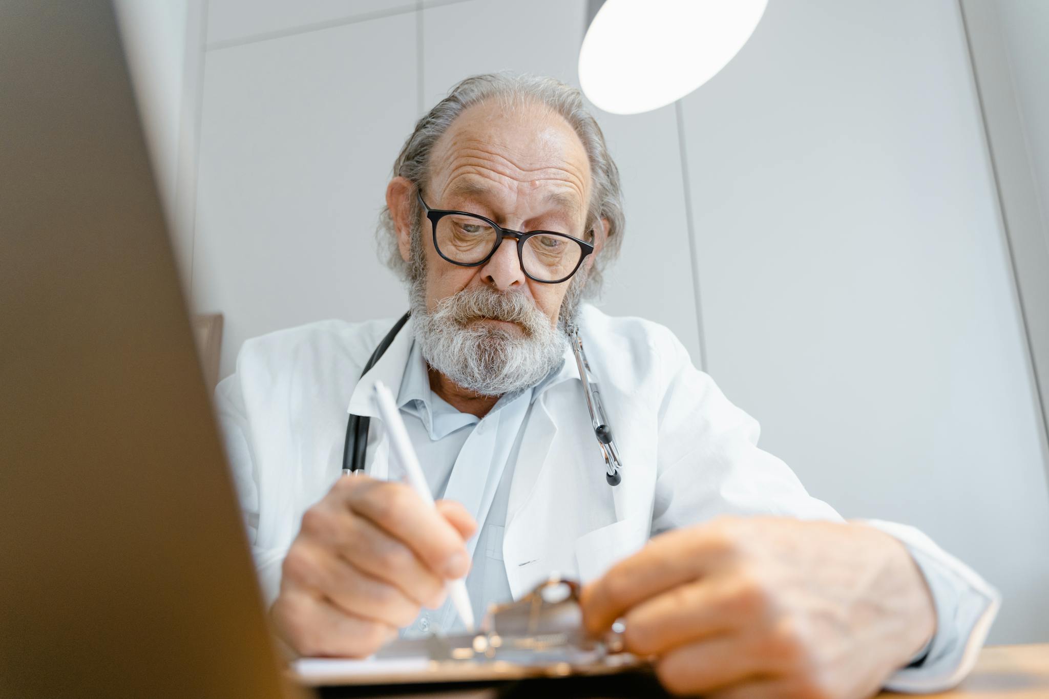 Senior doctor writing notes in a well-lit office setting.
